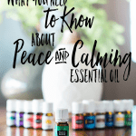 bottle of peace and calming essential oil with 11 other young living essential oils and a desert mist diffuser behind the oils. All are on a wooden table by a window with a plant