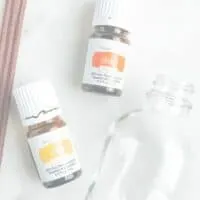 glass bottle laying next to brown reed diffusers and bottles of lemon and orange essential oils. Showing tools needed to make a reed diffuser