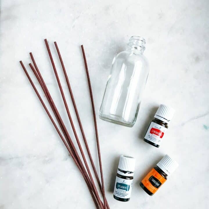 empty glass bottle lying next to reed diffusers and essential oil bottles of lemongrass, tangerine and spearmint. Showing what is needed to make DIY reed diffusers