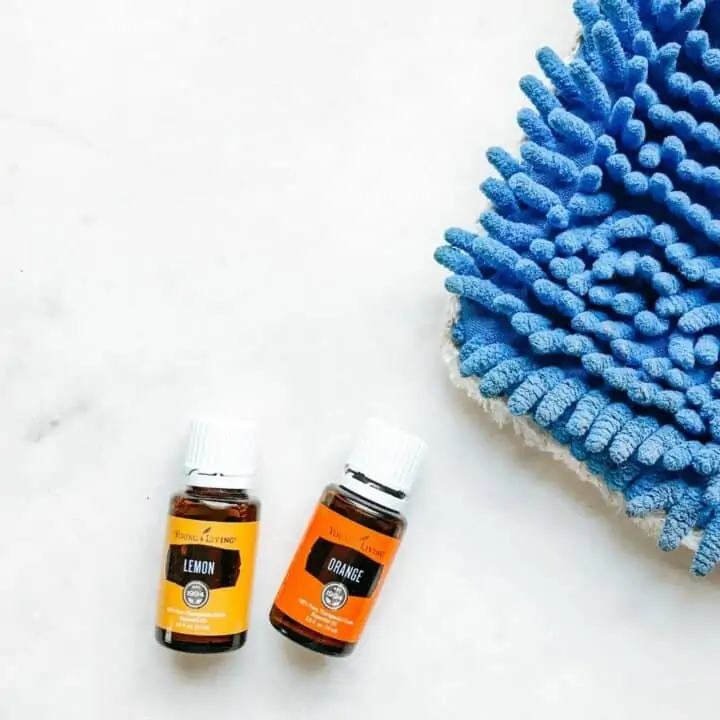 Lemon and Orange essential oils with a mop head on a white surface. Showing they are tools to make a homemade wood floor cleaner.