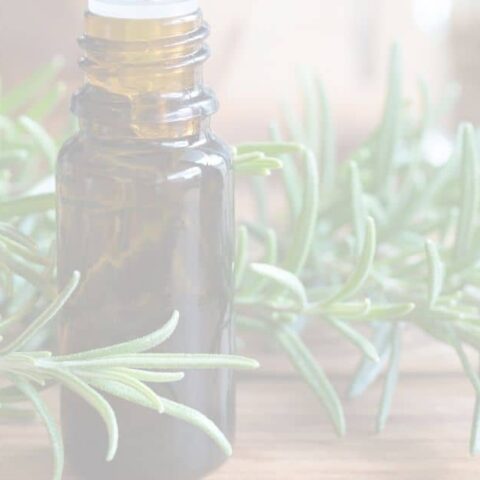 amber bottle of Rosemary essential oil surrounded by fresh rosemary